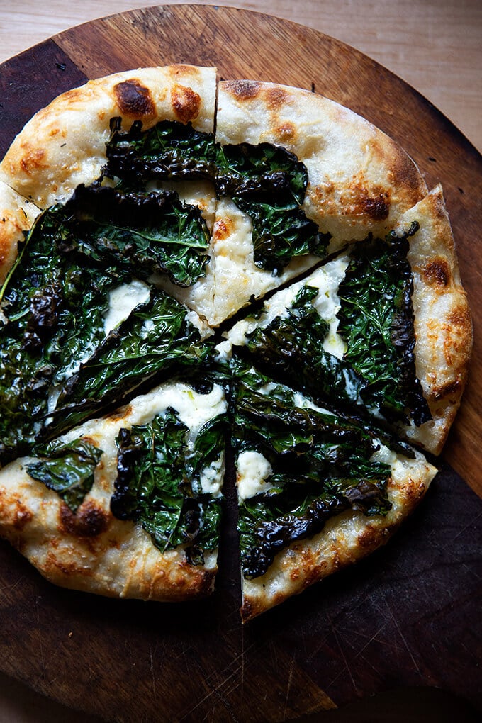 Sourdough kale and creme fraiche pizza on a board, cut into pieces.