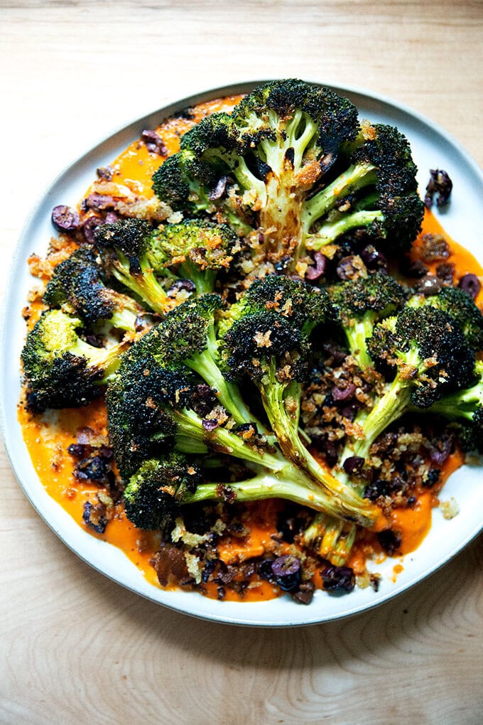 A plate of roasted broccoli steaks on tomato sauce topped with olive bread crumbs.