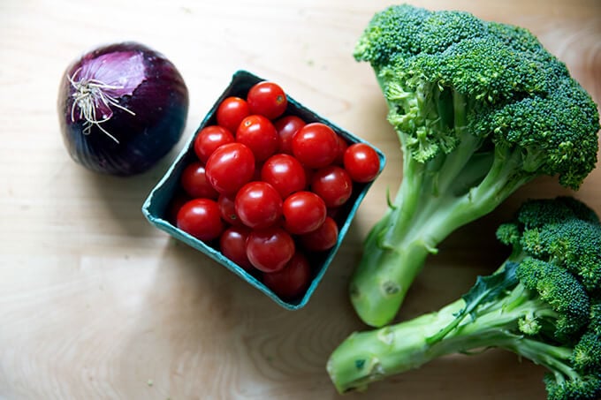 An onion, pint of cherry tomatoes and two heads of broccoli on a kitchen counter.