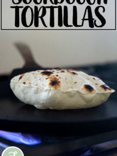 A sourdough flour tortilla cooking in a skillet stovetop.