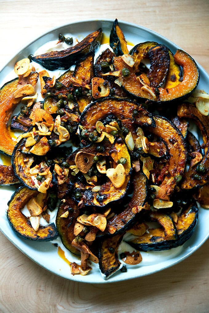 A plate of roasted Kabocha squash atop lemony yogurt sauce and sizzling garlic, capers, and Calabrian chili paste.