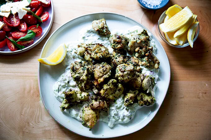 A plate of chicken souvlaki aside tomato salad and lemon.