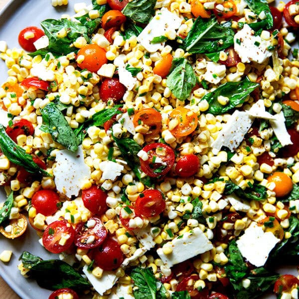 A platter topped with a raw corn salad made with tomatoes, feta, and lots of herbs.