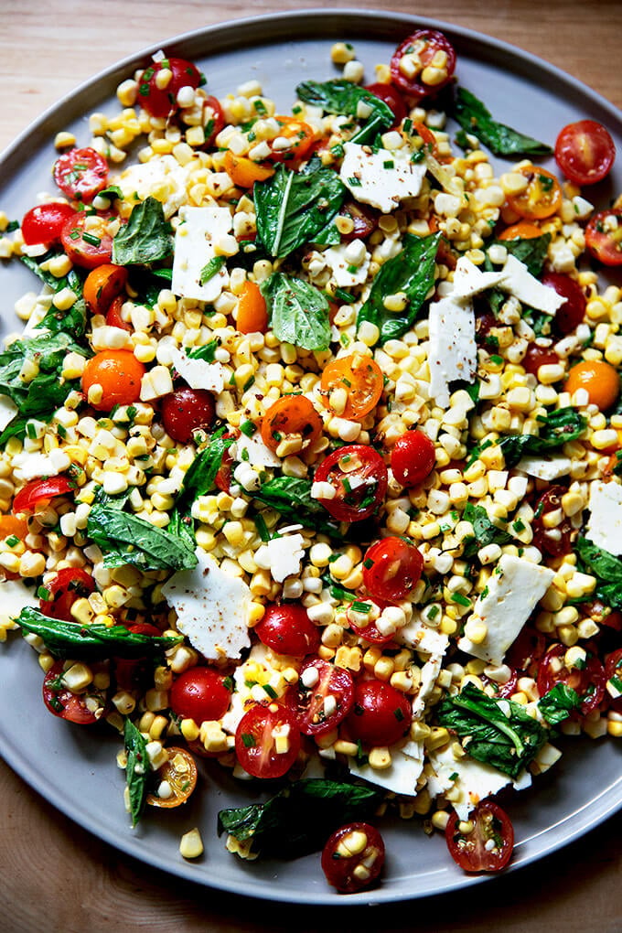 A platter topped with a raw corn salad made with tomatoes, feta, and lots of herbs.