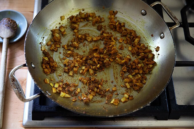 A skillet on the stovetop holding curry spiced onions, garlic, and ginger.