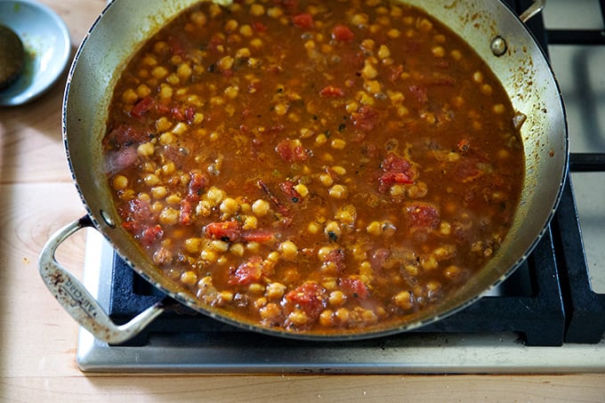 A skillet on the stovetop holding curry-spiced chickpeas and tomatoes.