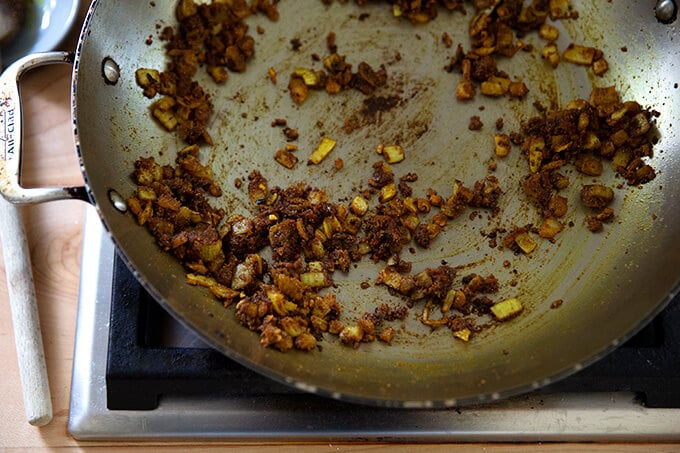 A skillet on the stovetop of sautéed onions, garlic, ginger, and curry spices.