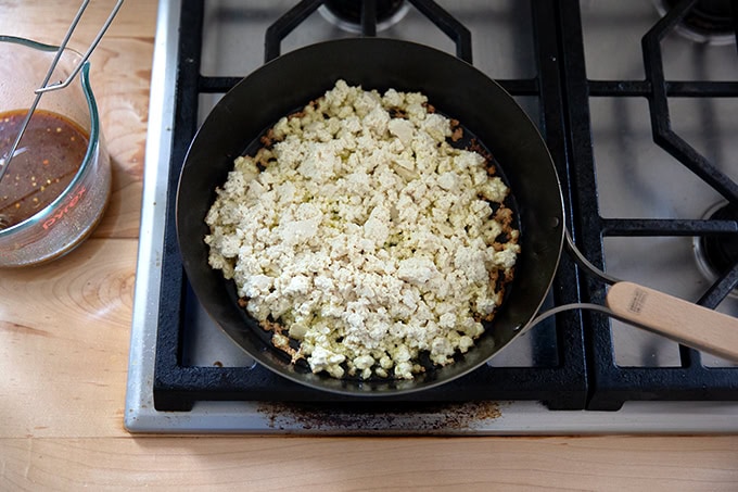 A skillet filled with hot oil and tofu crumbles.