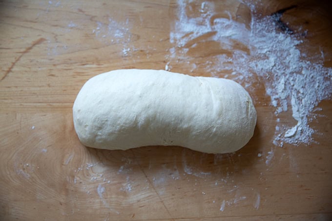 Coiled sandwich bread dough on a floured work surface.