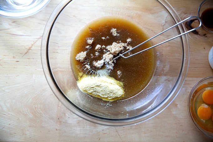 A bowl with maple syrup and melted butter whisked together with brown sugar, cornmeal, and salt added.