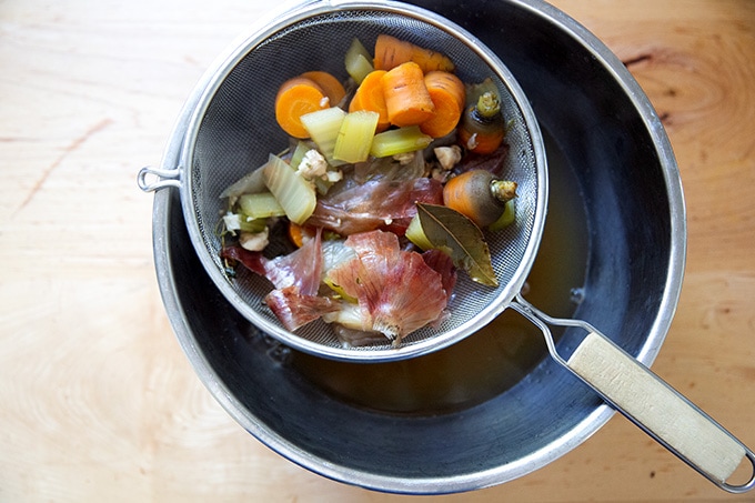 Drained vegetables in a colander over a bowl holding vegetable stock.