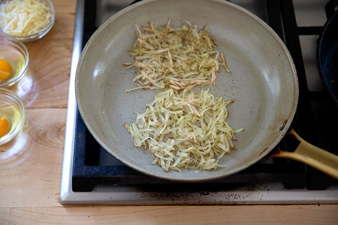 A skillet holding grated potatoes in two small piles.