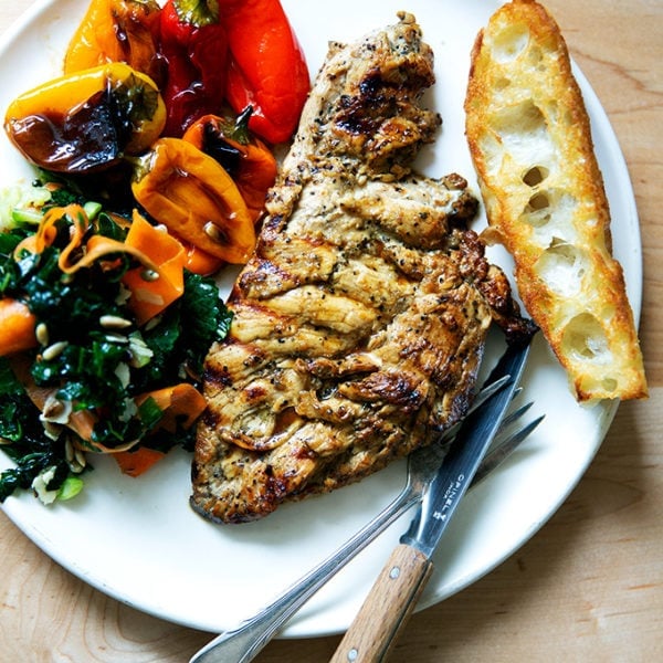 Grilled chicken breast on a plate aside bread, peppers, and salad.