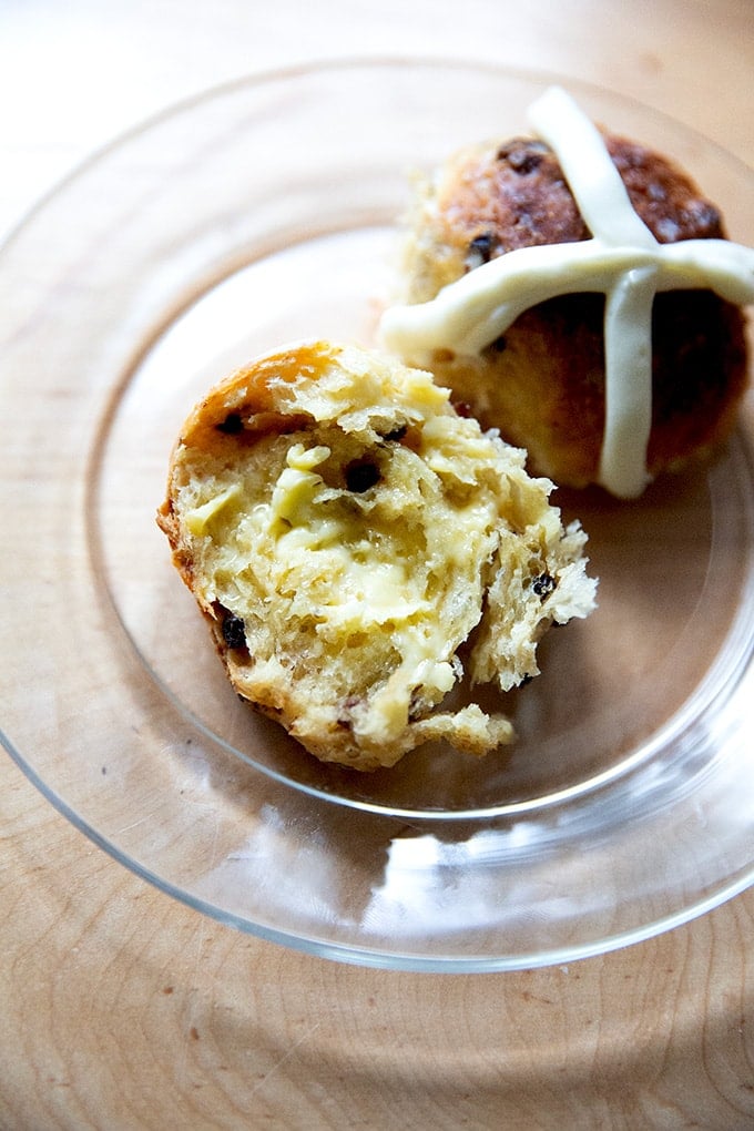 A buttered and halved hot cross bun on a plate.