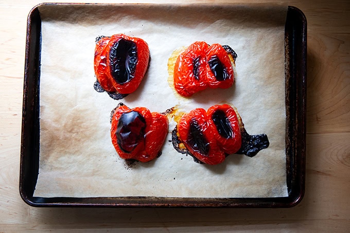 A sheet pan topped with 4 halved roasted red peppers.