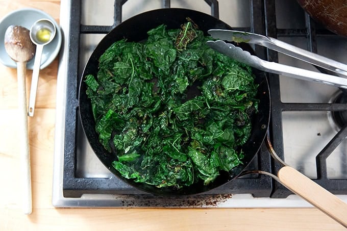 Kale sautéing in a skillet on the stovetop.