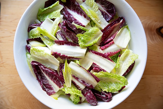 A large white serving bowl filled with lettuces dressed in Caesar dressing.