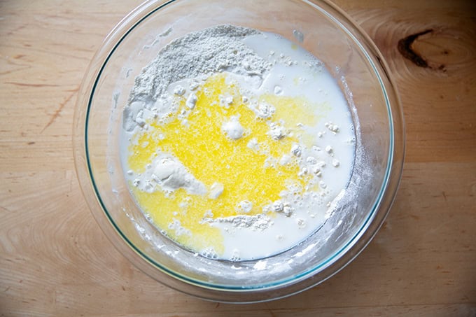 Butter and milk added to the dry ingredients to make sandwich bread in a large glass bowl.