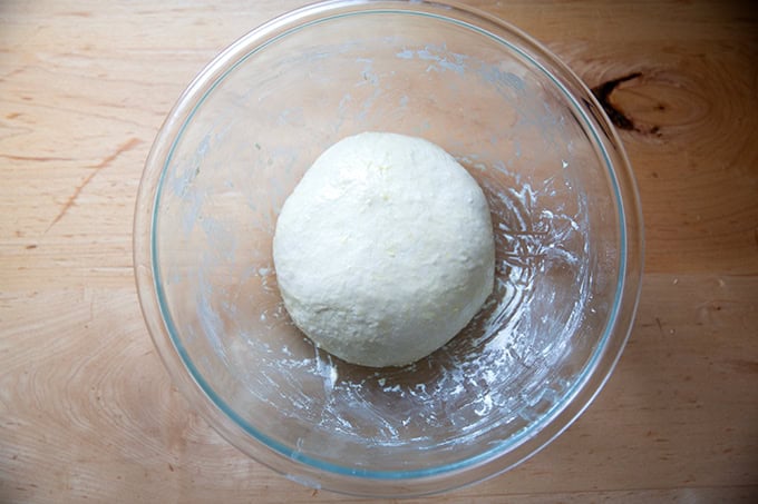 An oiled ball of soft sandwich bread in a large glass bowl.