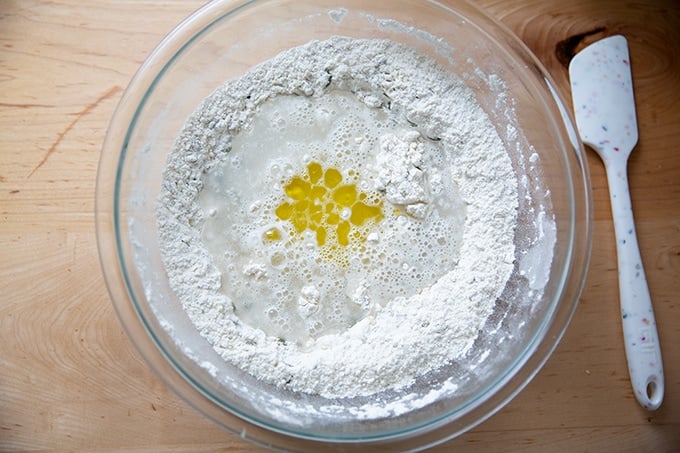 A bowl filled with the ingredients to make three seed bread aside a spatula.