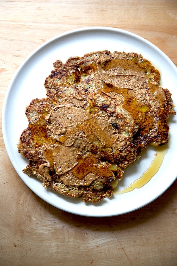 Banana-oat pancakes on a plate with almond butter and maple syrup.