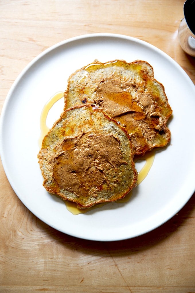 Banana-oat pancakes on a plate with almond butter and maple syrup.