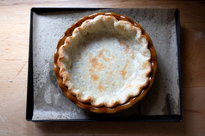 A parbaked pie crust on a parchment-lined sheet pan.