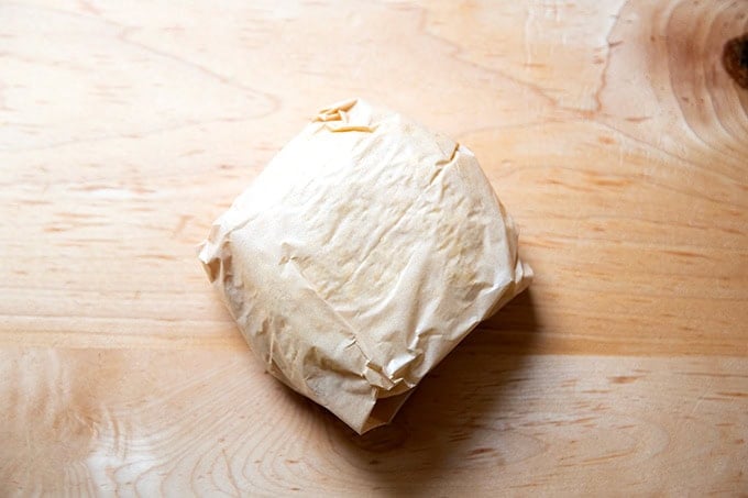 A round of pie dough wrapped in parchment paper.