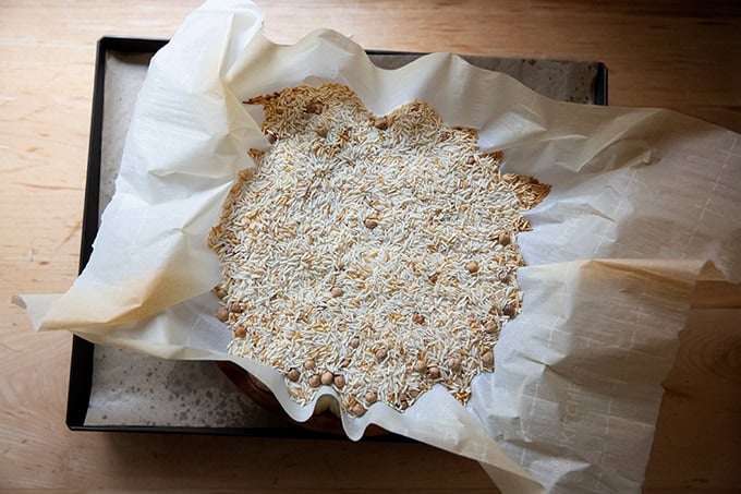 An overhead shot of pie weights — a mix of dried rice and chickpeas — filling a parchment-lined pie plate.