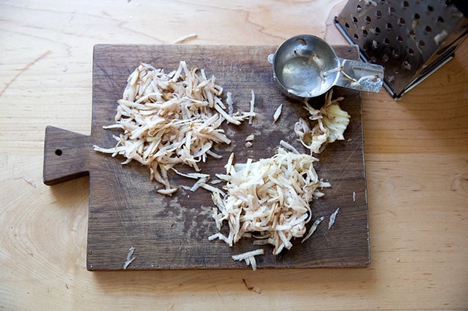 Two piles of grated potato on a cutting board.