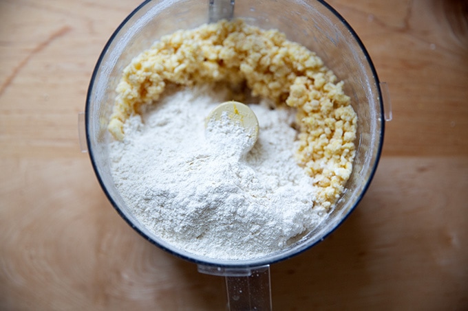 A food processor filled with the ingredients to make lemon-almond snowball cookie dough, partly blended.