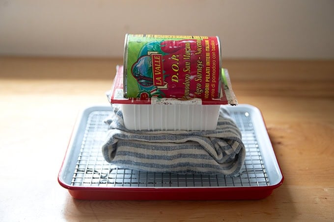 A can of tomatoes weighing down a cloth-wrapped block of tofu.