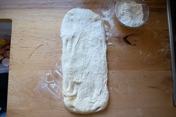 Stretched out sandwich bread dough on a floured work surface, ready to be coiled up.