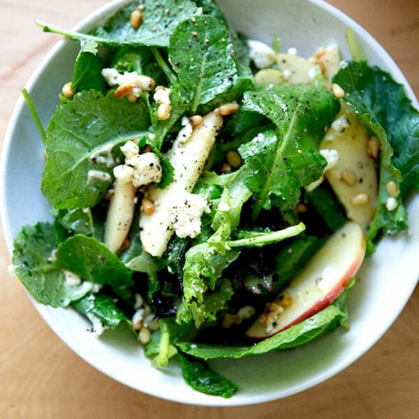 A fall salad of greens, pine nuts, goat cheese, and apples in a bowl.