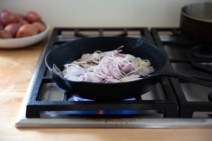 Shallots in a cast iron skillet on the stovetop.