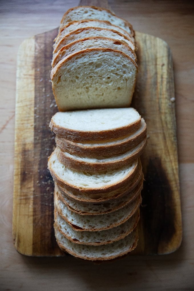 A loaf of soft sandwich bread, sliced on a cutting board.