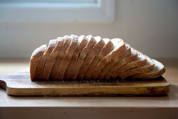 A loaf of soft sandwich bread, sliced on a cutting board.