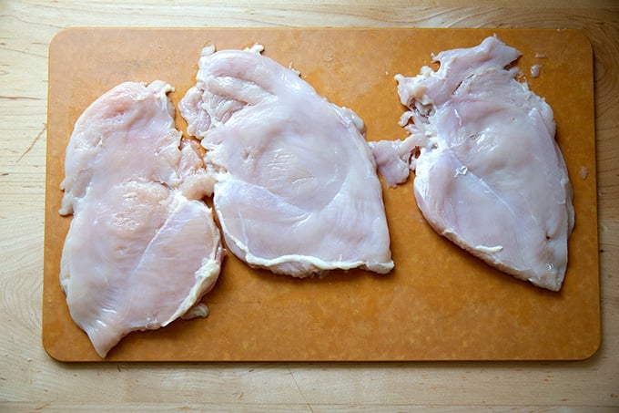 Three flattened chicken breasts on a cutting board.