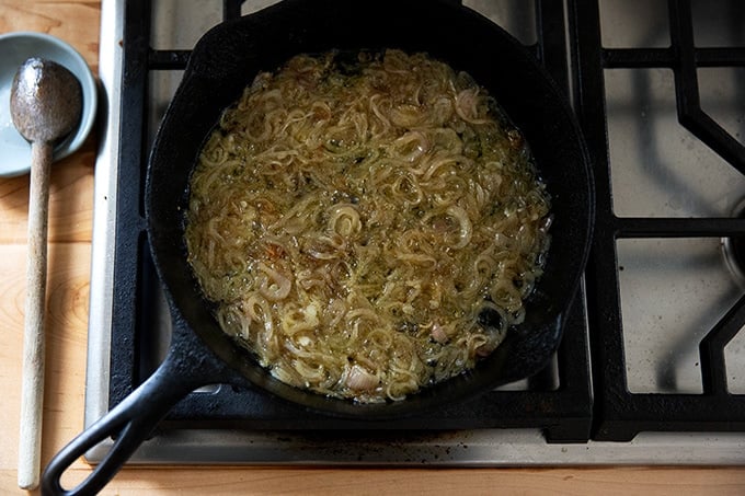 Shallots sizzling in a cast iron skillet on the stovetop.
