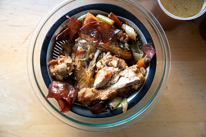 The scraps of turkey stock in a strainer set in a large bowl.
