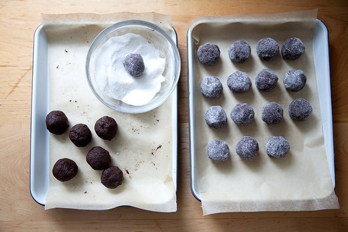 Chocolate crinkle cookie dough balls being rolled in sugar.