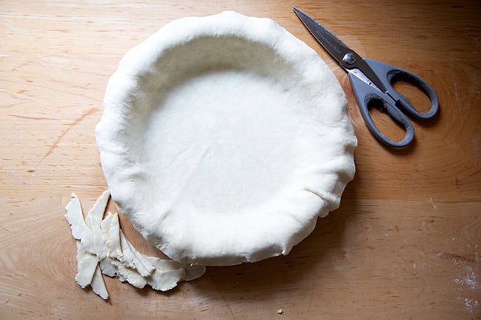 A pie plate fitted with pie dough with the overhanging edges trimmed.