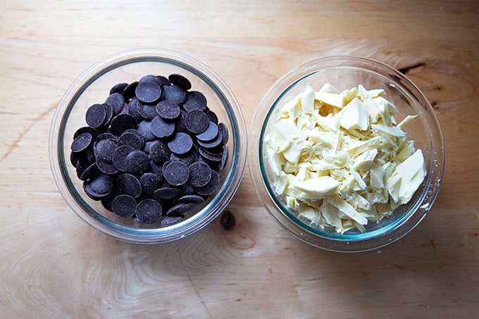 Two bowls of chocolate: one of dark chocolate disks, the other of chopped white chocolate.
