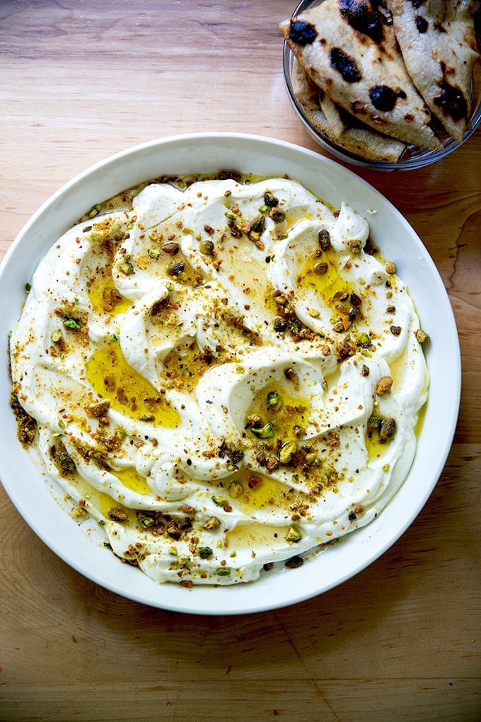A platter of whipped ricotta with honey, olive oil, and pistachios aside a bowl of bread.