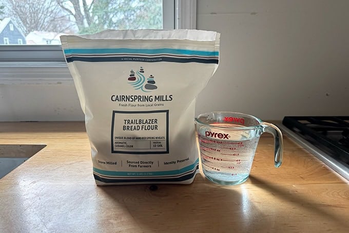 A bag of Cairnspring Mills Trailblazer Bread Flour aside a 2-cup Pyrex measure filled with water.