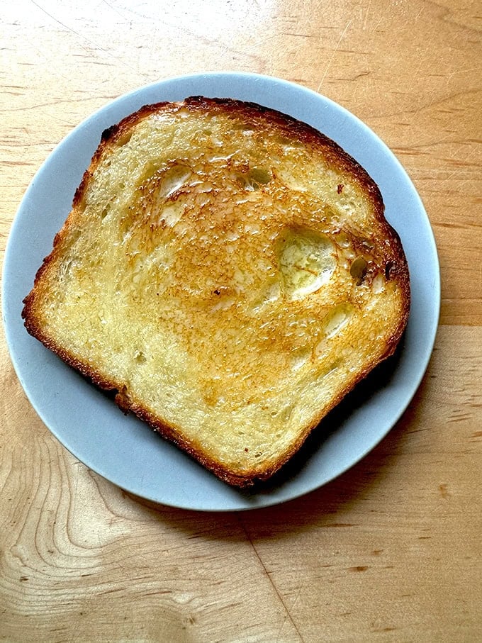 A slice of sourdough discard toasting bread, toasted and buttered on a plate.