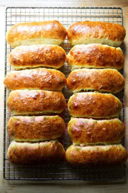 Twelve just-baked brioche hot dog buns on a cooling rack.