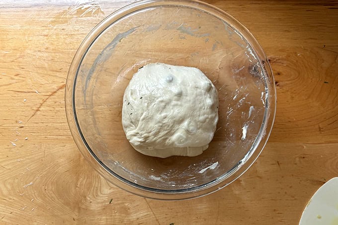 Rosemary olive sourdough dough folded and in a large glass bowl.