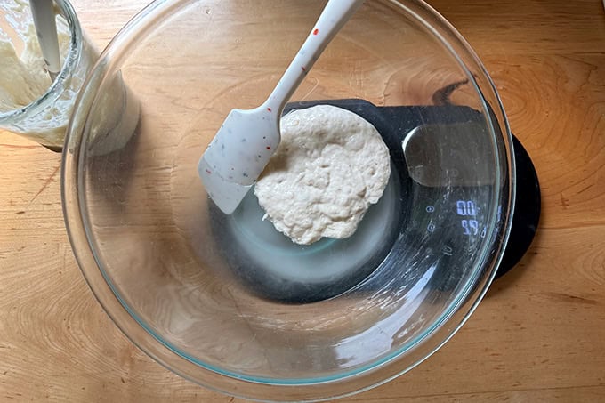 A bowl with water, salt and sourdough starter set on a scale.