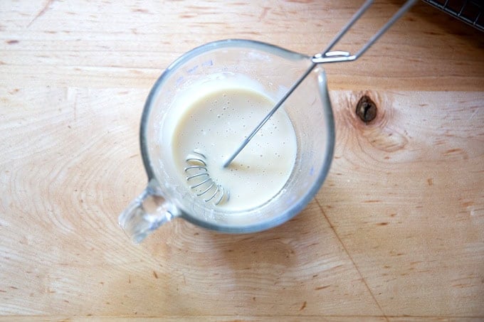 A small liquid measure filled with a confectioners sugar glaze for cinnamon-sugar focaccia.